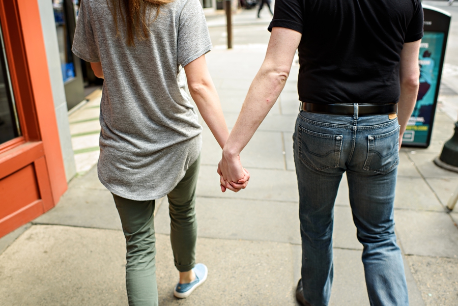 An engaged couple hold hands and walk the streets of Philadelphia near City Hall.